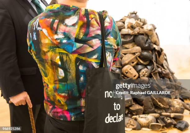 Un couple regarde un amoncellement de masques en bois africain, la femme portant un sac avec une inscription 'Nothing to declare' au Grand Palais...