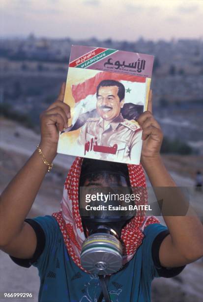 Palestinien portant un masque à gaz dans les territoires occupés pendant la crise du Golfe montrant un portrait de Saddam Hussein le 26 août 1980 en...