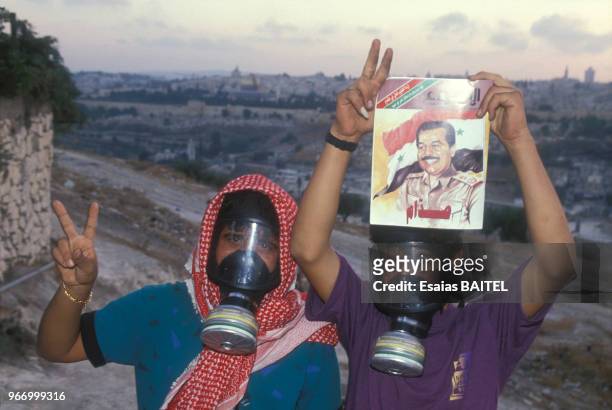 Palestiniens équipés de masques à gaz dans les territoires occupés pendant la crise du Golfe brandissant un portrait de Saddam Hussein le 26 août...