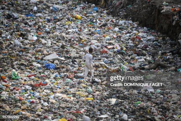 This photo taken on May 30, 2018 shows a rag picker walking along a sewage drain canal full of garbage in the Taimur Nagar slum area in New Delhi. -...