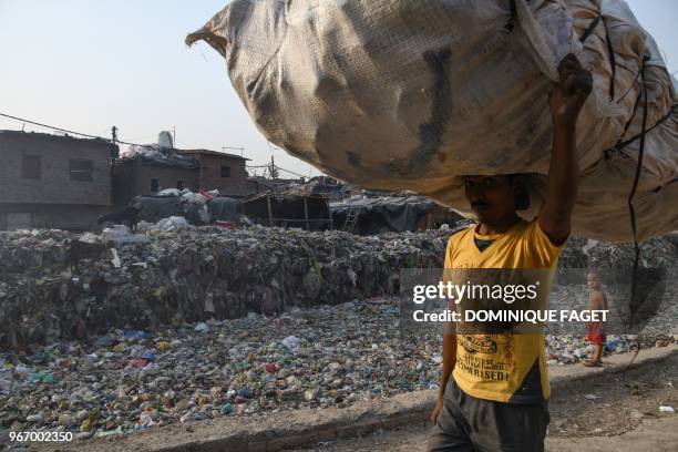 This photo taken on May 30, 2018 shows a man carrying a bag containing plastic recyclable items next to a sewage drain canal full of garbage in the...