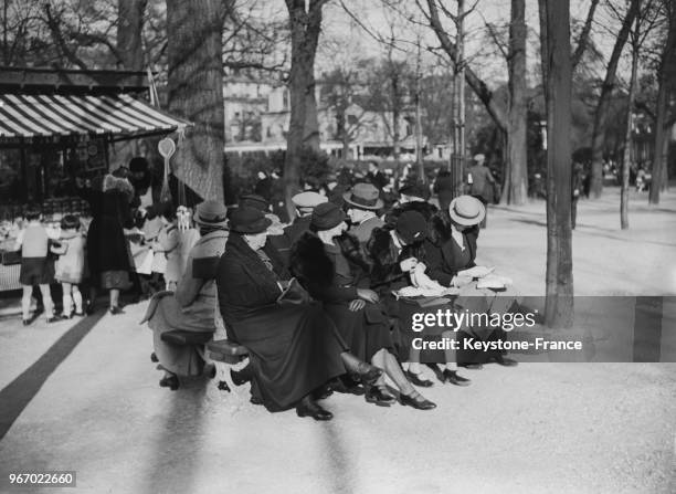 Dans un jardin parisien, des femmes assises sur un banc prennent le soleil pendant que les enfants jouent, à Paris, France le 21 mars 1935.