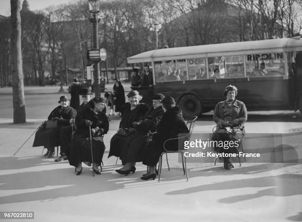 Des femmes prennent le soleil assises sur des chaises installées sur le trottoir, à Paris, France le 21 mars 1935.