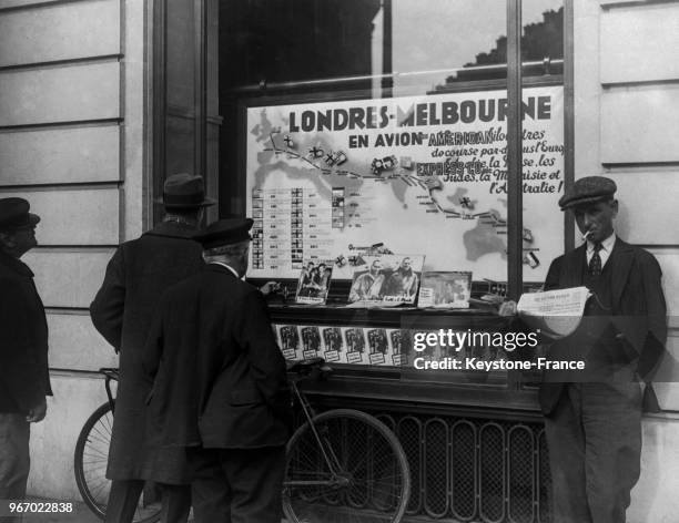 Des hommes regarde une carte sur laquelle est tracé l'itinéraire de la célèbre course aérienne exposée dans la vitrine d'une agence de voyages, en...