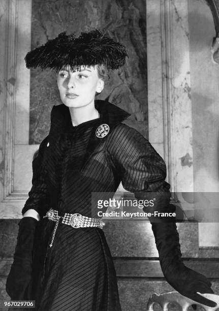 Mannequin portant un modèle Jean Dessès: une robe en organdi noir rayé avec une ceinture copiée sur un bijou ancien et un chapeau garni de plumes...
