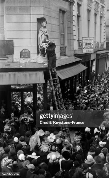 Montée sur une échelle, une catherinette fleurit la statue de la Sainte-Catherine, à Paris, France le 25 novembre 1933.