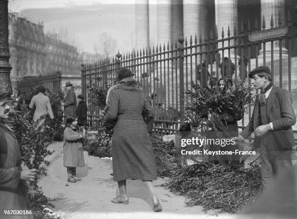 Près de l'église de la Madeleine, les vendeurs et vendeuses de rameaux de buis trouvent de nombreux clients, à Paris, France le 25 mars 1934.