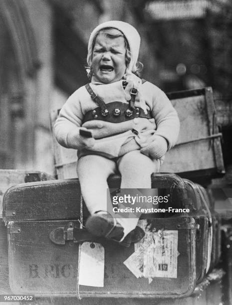 Un bébé en pleurs, assis sur une valise dans une gare à Paris, France le 30 mars 1934.