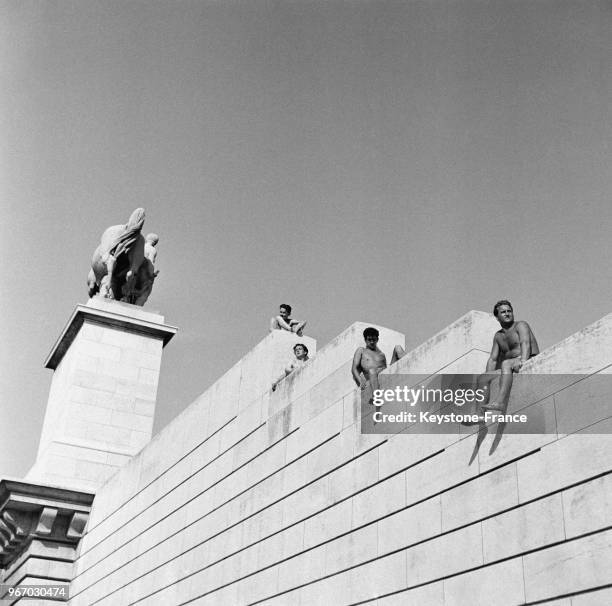 Des jeunes gens, en maillot de bain, se font bronzer sur le muret du Trocadéro, à Paris, France le 25 juillet 1953.