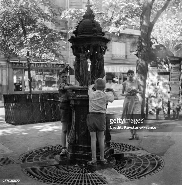 Garçons se rafraichissant à une fontaine, à Paris, France le 27 juillet 1956.