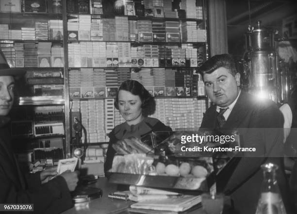 Monsieur et Madame Magne, débitants de la rue de Rivoli, derrière leur comptoir, un client tient en main un billet de la Loterie, à Paris, France le...