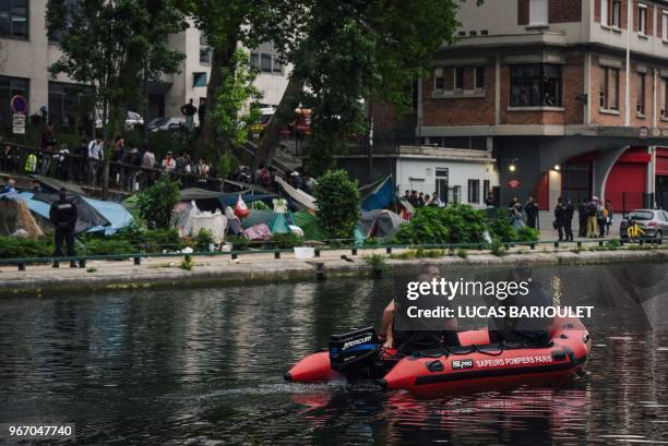 Firefighters sail an inflatable boat next to a makeshift camp during its evacuation by police, along the Canal de Saint-Martin at Quai de Valmy in...