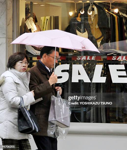 Japan-China-economy-society,FOCUS by Hiroshi Hiyama Shoppers walk past an apparel shop displaying a large "sale" sign in Tokyo on February 15, 2010....