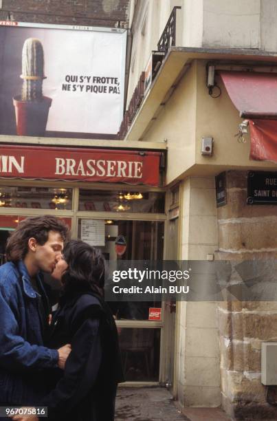 Jeune couple s'embrassant dans la rue devant une affiche de prévention pour le port du préservatif, à Paris, le 24 février 1989, France.