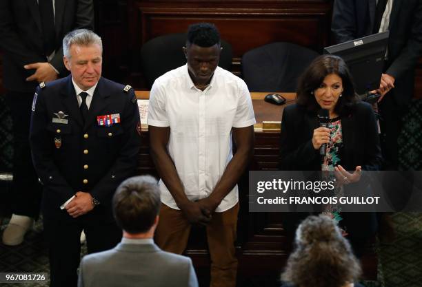 Malian migrant Mamoudou "Spider-Man" Gassama stands by Paris' mayor Anne Hidalgo speaking and the chief of the Paris' fire Brigade General...