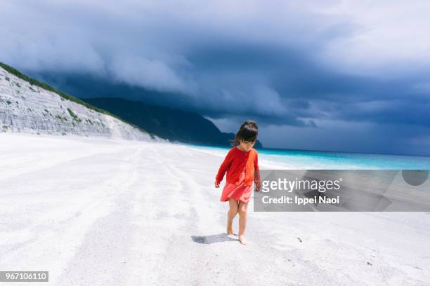 Little girl walking on white sand beach while storm clouds approach