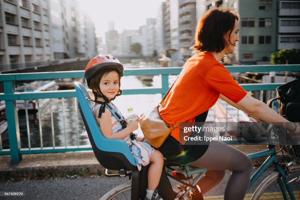 Mother riding a bicycle with a toddler girl in urban city, Tokyo