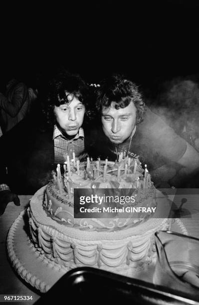 Johnny Hallyday fête son 33ème anniversaire. Il souffle les bougies de son gateau avec Gérard Lenorman, le 16 juin 1976 à Thoiry, France.