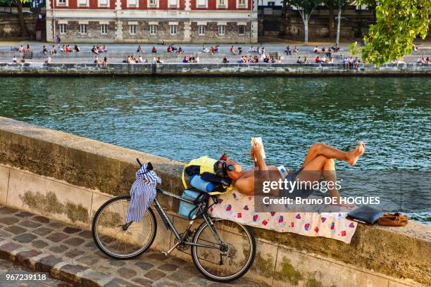 Un homme allongé avec un livre et un casque écouteur sur le quai d'Orléans de l'Île Saint-Louis, 20 juin 2017, Paris, France.