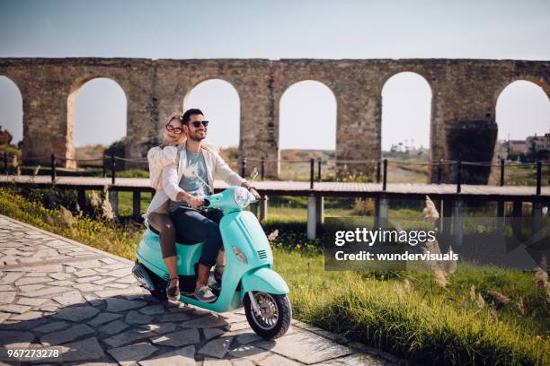 young romantic couple riding retro scooter in italian town - couple scooter stock pictures, royalty-free photos & images