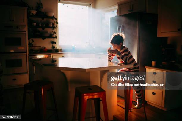 boy sitting in kitchen eating his breakfast in morning light - boy pajamas cereal stock pictures, royalty-free photos & images