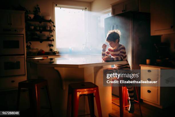 boy sitting in kitchen eating his breakfast in morning light - boy kitchen stockfoto's en -beelden