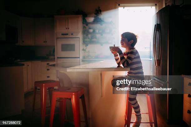 boy sitting in kitchen eating his breakfast in morning light - boy pajamas cereal stock pictures, royalty-free photos & images