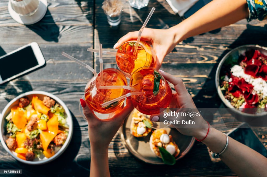 Overhead view of three women making a celebratory toast with Spritz cocktails