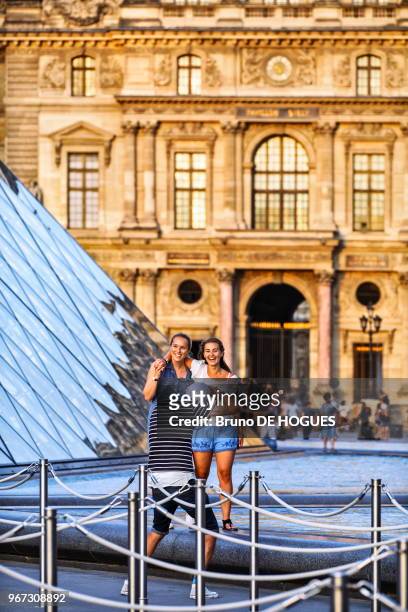 Deux jeunes femmes se faisant prendre en photo devant la Pyramide du Louvre, 15 juin 2017, Paris, France.