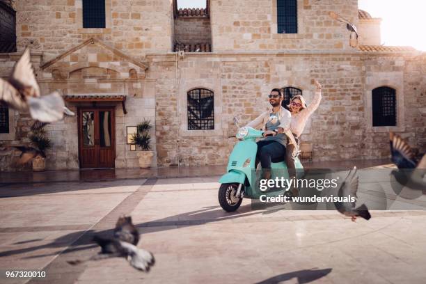 joven pareja teniendo diversión vespa vintage del montar a caballo en la ciudad europea - holiday scooter fotografías e imágenes de stock