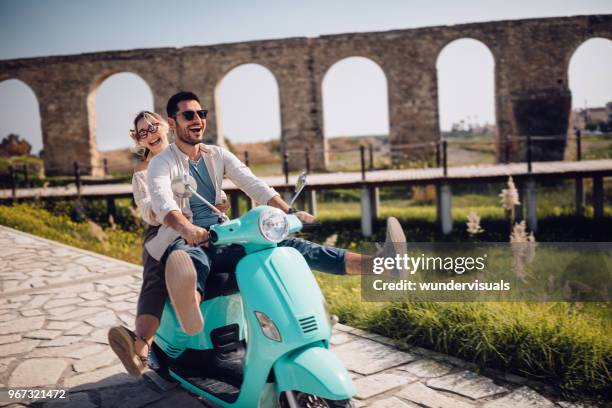 jóvenes felices pareja scooter retro del montar a caballo en antigua ciudad mediterránea - holiday scooter fotografías e imágenes de stock