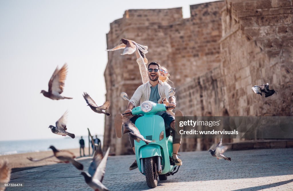 Young couple having fun riding scooter in old European town