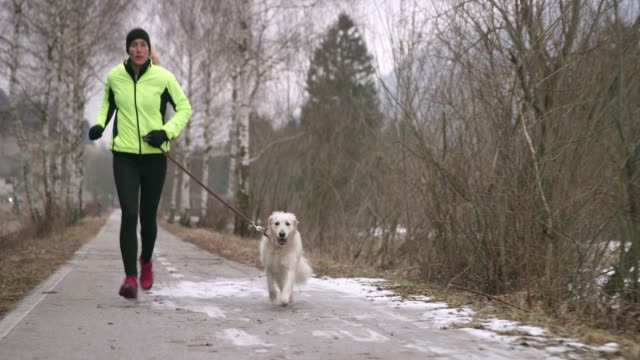 Young Caucasian woman running on a walkway in winter with her dog