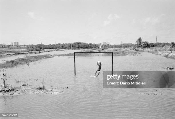 Child playing football during a high tide in the favela 'Ilha de Deus' , Recife, Brazil, 2002. A favela is the Brazilian equivalent of a shanty town,...