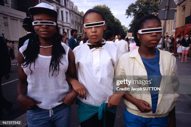 Trois jeunes filles noires portent des lunettes de soleil insolites lors du carnaval jamaicain de Notting Hill le 28 août 1983 à Londres, Royaume-Uni.