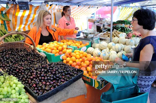 Une vendeuse de primeurs devant un étal de cerises, d'abricots et melons tend un abricot à une cliente au marché Edgard Quinet, 17 juin 2017, Paris,...