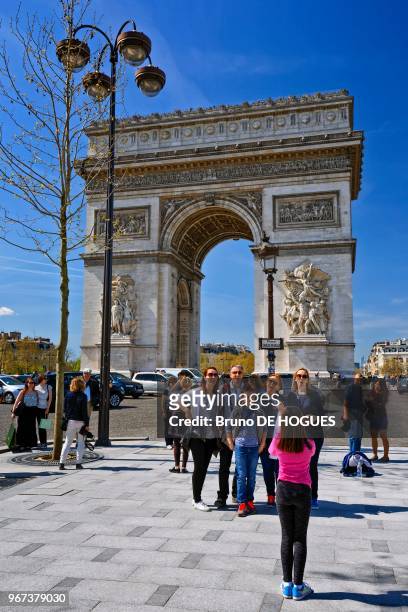 Des touristes se prenant en photo devant l'Arc de Triomphe à Paris.