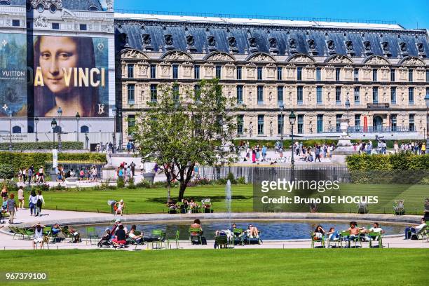 Des gens bronzant dans le Jardin des Tuileries devant le Louvre et le portrait de La Joconde, 26 mai 2017, Paris, France.