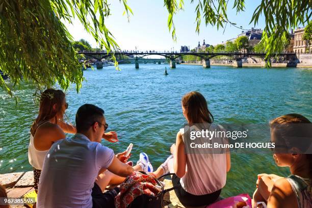 Gens assis sur le quai à la pointe du Vert-Galant sur l'île de la Cité, face au Pont des Arts et au Louvre, 25 mai 2017, Paris, France.