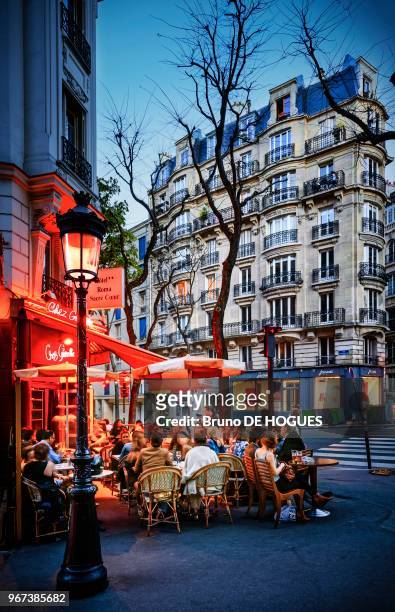 Des gens à la terrasse d'un café-restaurant de la Butte Montmartre à la tombée de la nuit, Paris.