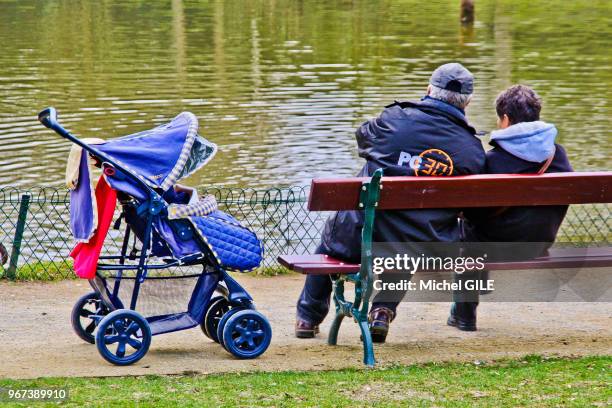 Couple de personnes agées sur un banc à cote d'une poussette au jardin des plantes, Le Mans, France.