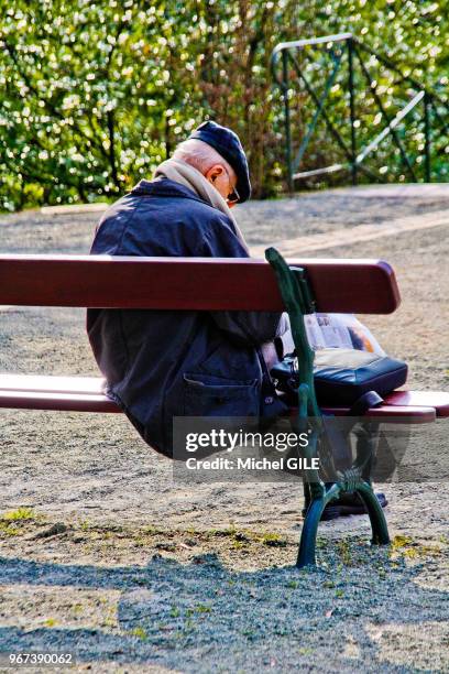 Homme age sur un banc avec un journal au jardin des Plantes, Le Mans, France.