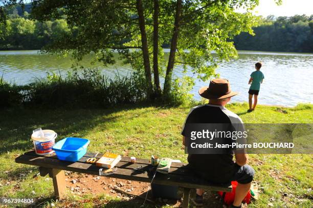 Petit garçon qui pêche et son grand-père assis sur un banc au bord du lac du Causse, 17 juillet 2017, près de Brive la Gaillarde en Corrèze, Nouvelle...
