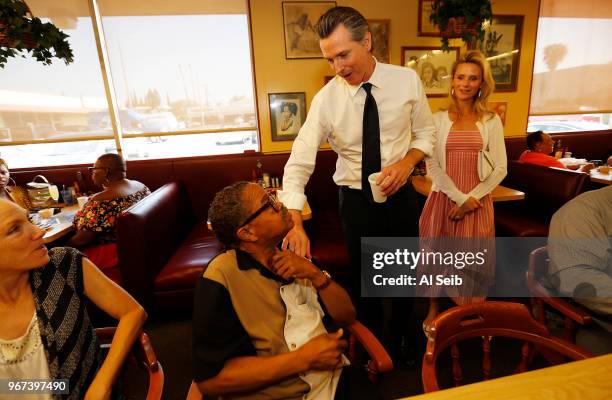 Gavin Newsom with his wife Jennifer Siebel Newsom, right, greet Ronnie Breaux, left, one of several morning diners at The Serving Spoon Restaurant in...