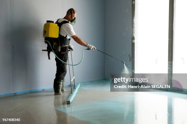 Ouvrier du bâtiment équipé de protections individuelles lors de la mise en ?uvre d'une chape de béton liquide, dans un chantier de construction de...