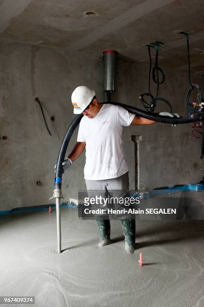 Ouvrier du bâtiment coulant une chape de béton liquide, dans un chantier de construction de logement.