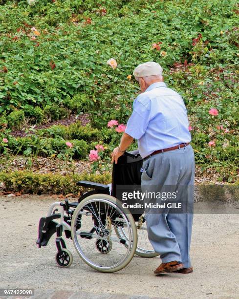Un homme âgée pousse un fauteuil roulant vide, 20 aout 2015, Jardin des plantes, Le Mans, France.