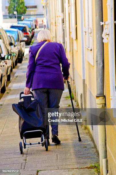 Femme agee avec canne roulant son caddie sur le trottoir, Le Mans, Sarthe, France.