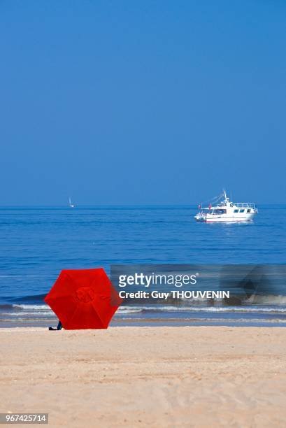 Parasol rouge sur la plage et bateau au loin, Trouville sur Mer, France.