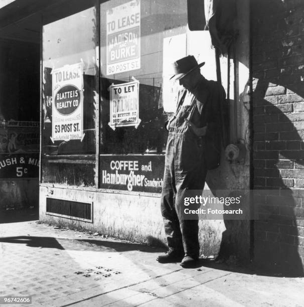 Unemployed man stands against a vacant store - with 'To Let' and 'To Lease' posters in the window - in a photograph by Dorothea Lange, on 'Skid Row',...